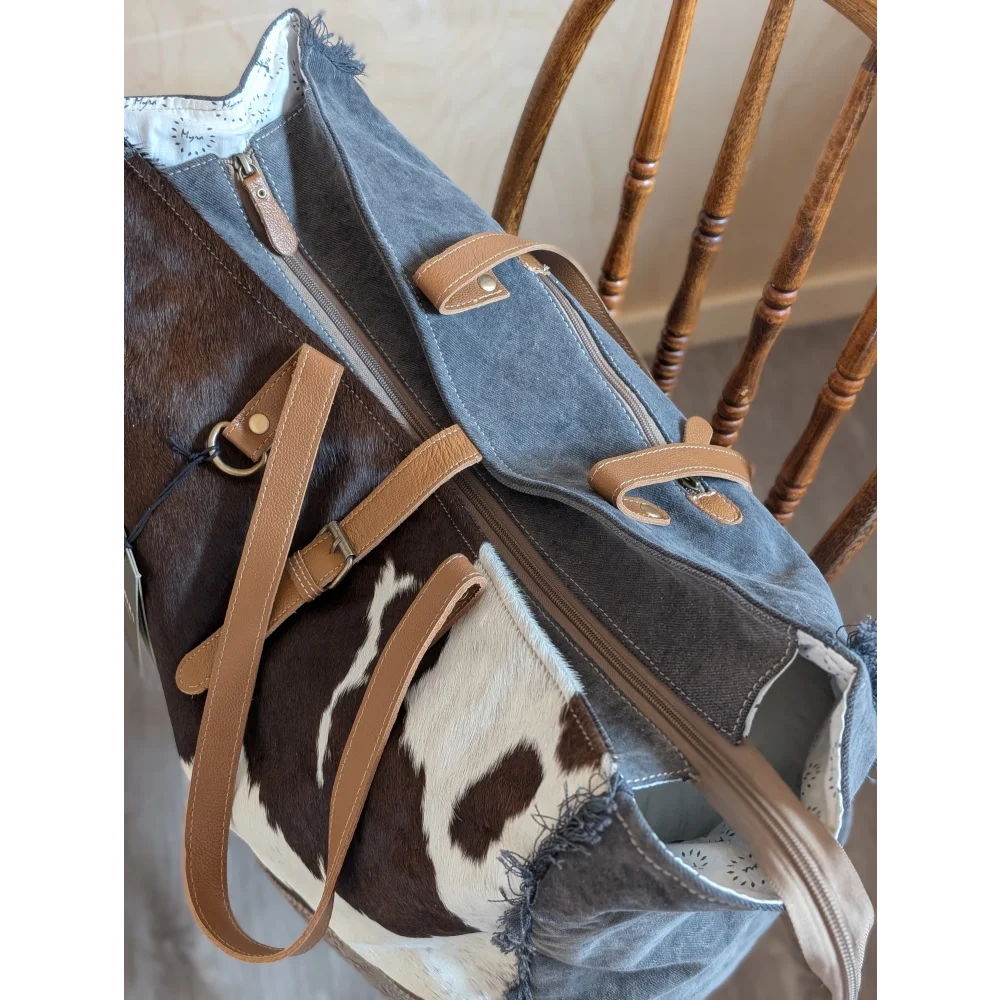 A stylish denim and cowhide matty affair canvas weekender bag with frayed edges and tan leather straps by angus oliver