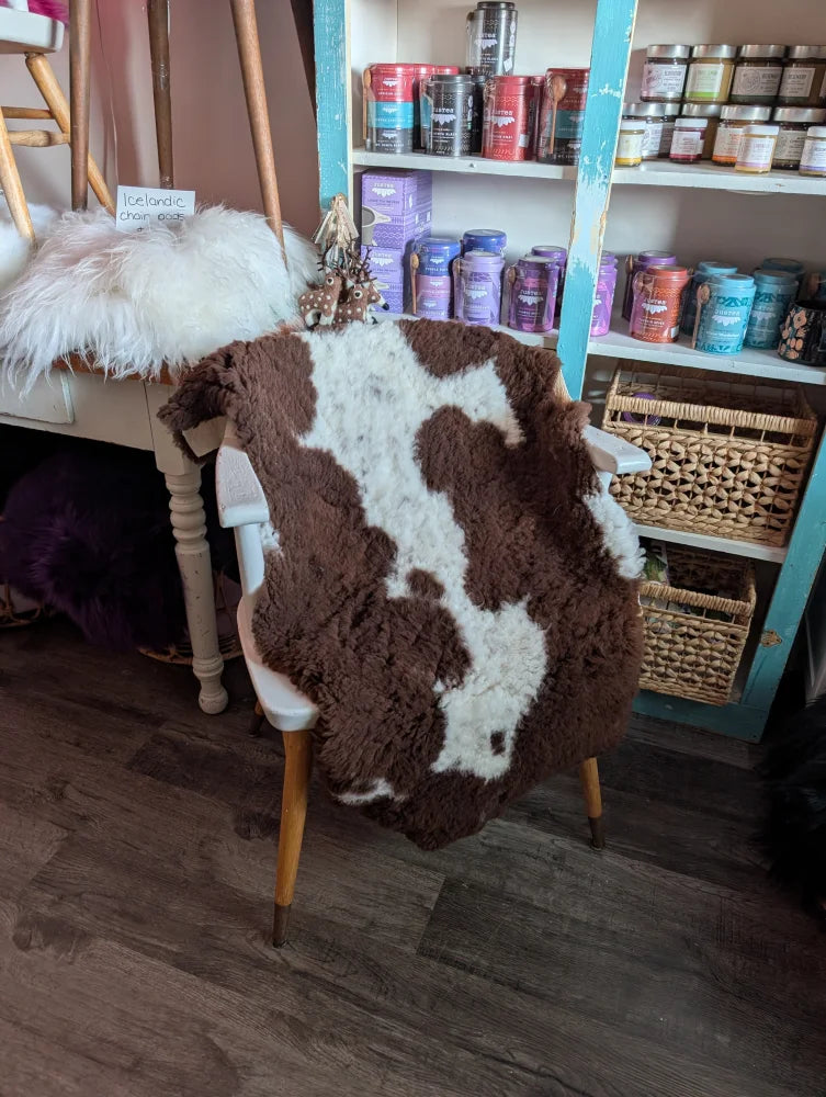 Brown and white highland spotted sheepskin grade a- rug draped over chair showcasing soft natural wool texture