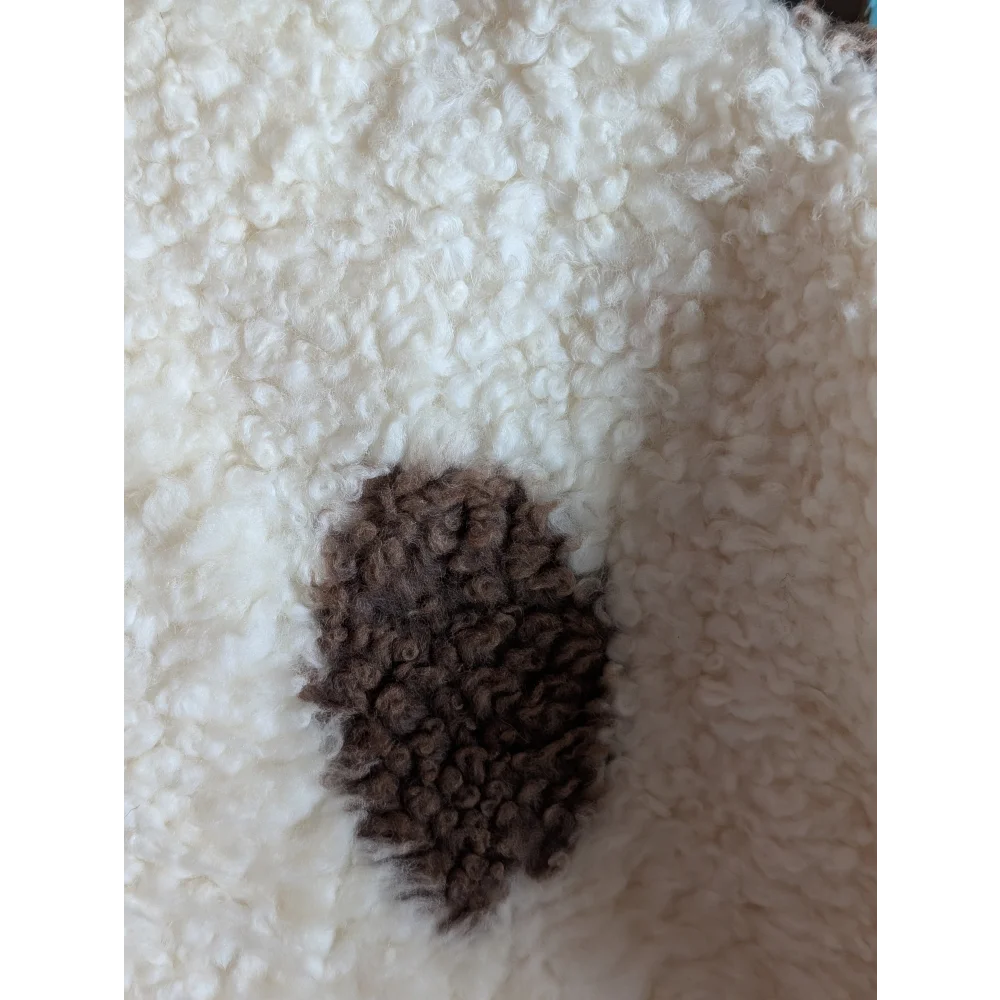A dark brown textured patch on a grade a- highland spotted sheepskin contrasts with the white fluffy fabric