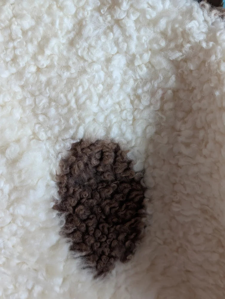 A dark brown textured patch on a grade a- highland spotted sheepskin contrasts with the white fluffy fabric