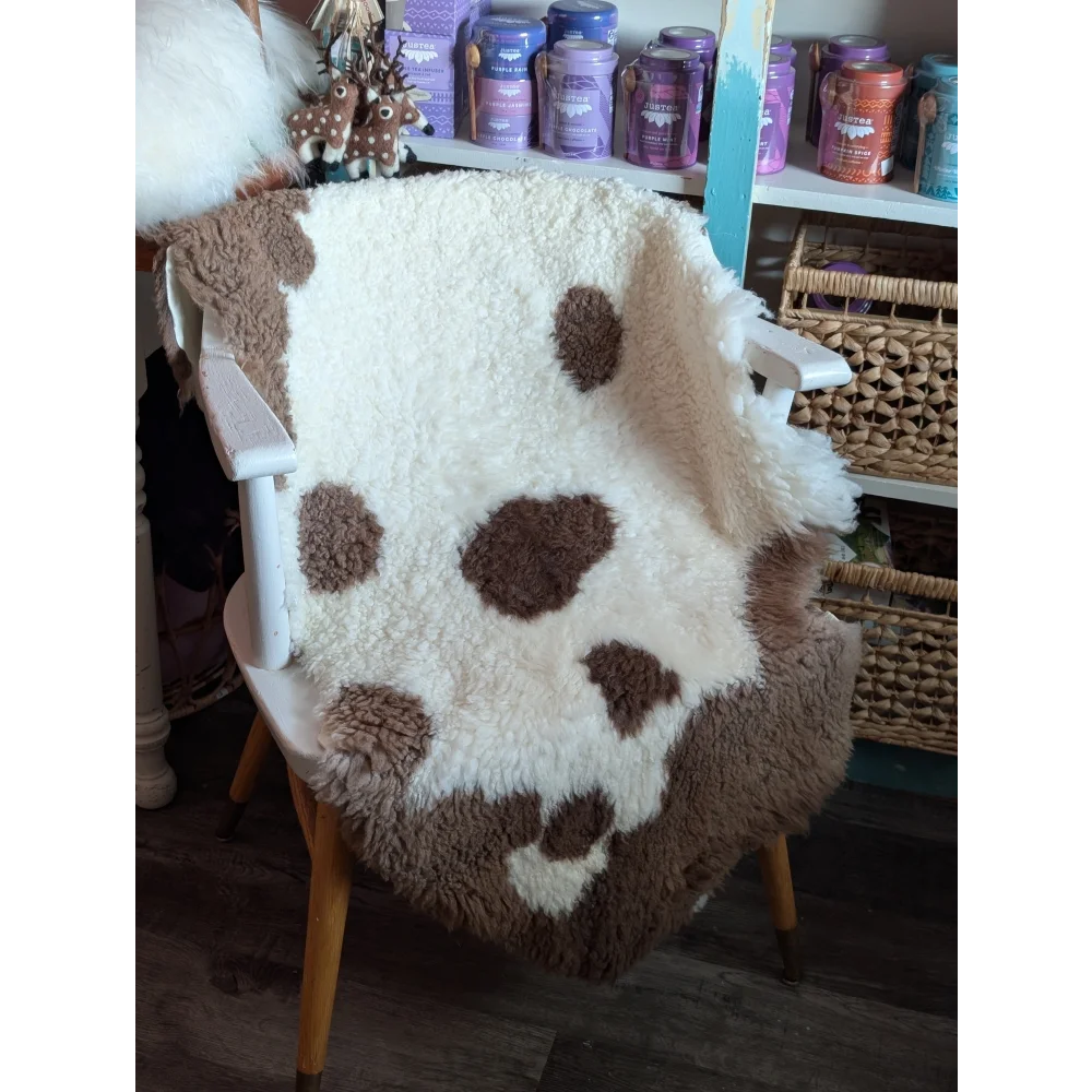 A cozy cream and brown highland spotted grade a sheepskin throw draped over a white chair