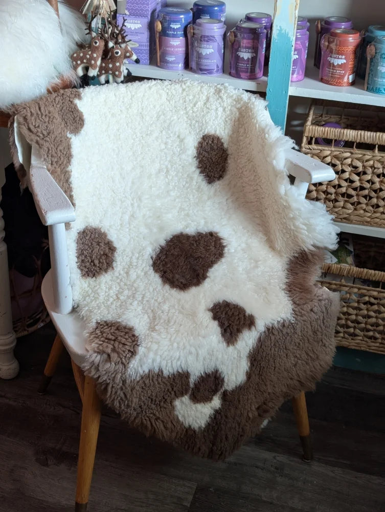 A cozy cream and brown highland spotted grade a sheepskin throw draped over a white chair