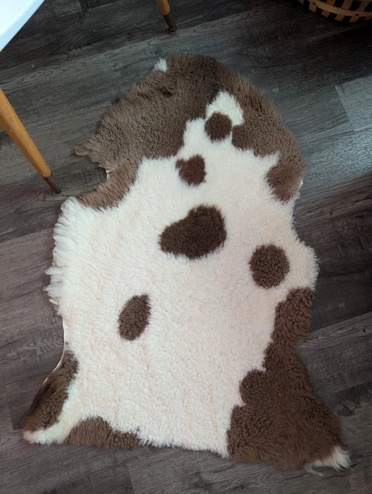 A plush grade a- highland spotted sheepskin rug with natural white and brown cow-print pattern