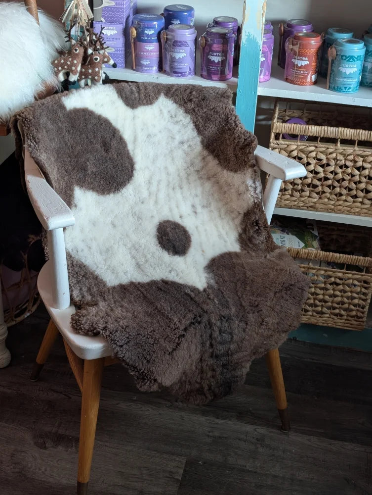 A cozy highland spotted grade a- sheepskin blanket with cow-print draped over a white wooden chair