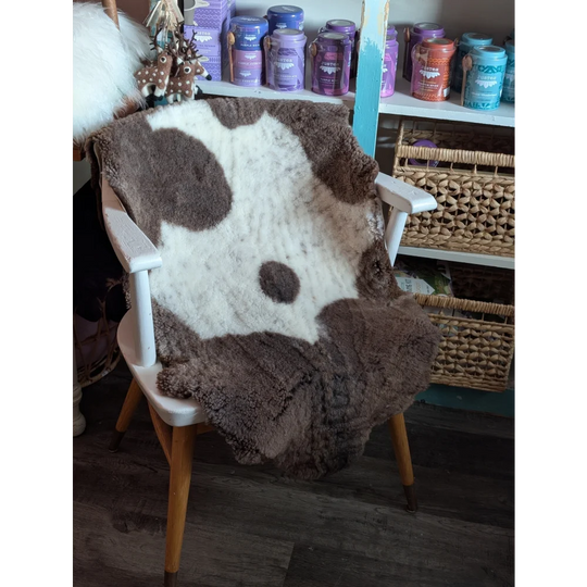 A cozy highland spotted grade a- sheepskin blanket with cow-print draped over a white wooden chair
