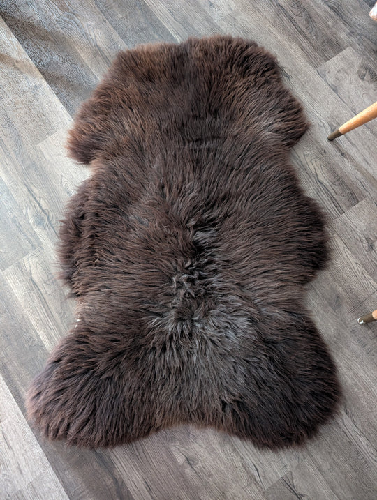 A plush extra large british sheepskin rug in dark brown with natural fluffy texture and irregular edges