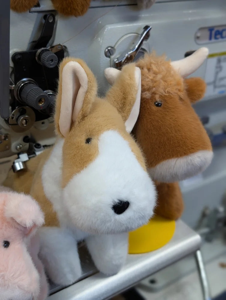 A plush tan and white rabbit with soft fur and stitched nose sitting by other stuffed animals on a sewing machine