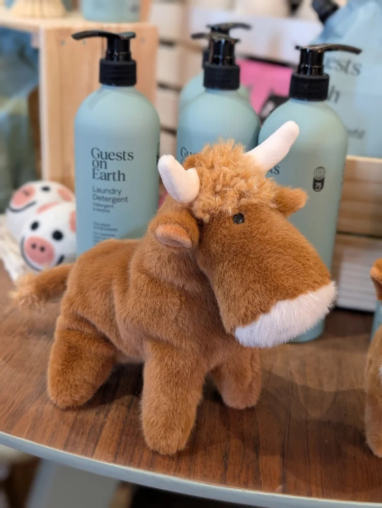 Adorable plush brown highland cow stuffed toy with white horns white muzzle and head fluff on wooden surface
