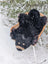 Adorable merino sheepskin black bear rug handmade plush with tan accents resting in a wicker chair outdoors in snowfall
