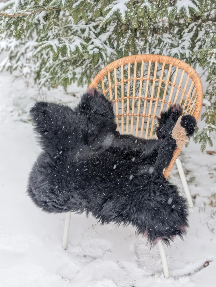Adorable merino sheepskin black bear rug black fluffy hand made throw draped over a wicker chair