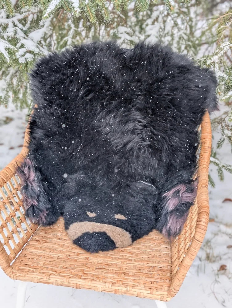 Adorable hand made merino sheepskin black bear rug with tan accents resting in a woven wicker basket