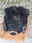 Adorable hand made merino sheepskin black bear rug with tan accents resting in a woven wicker basket