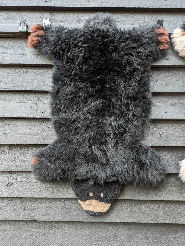 Adorable merino sheepskin bear rug in dark gray with tan paw pads and light brown snout perfect as a black bear decor piece