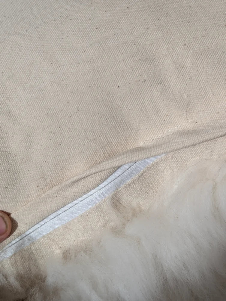 Beige canvas pillow with white zipper and fluffy white interior from adorable set of sheepskin cushions by angus oliver canada