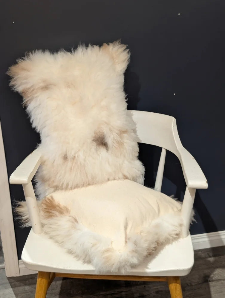Fluffy off-white sheepskin throw pillow with soft natural fur resting on a white wooden chair by angus oliver canada
