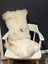 Fluffy off-white sheepskin throw pillow with soft natural fur resting on a white wooden chair by angus oliver canada