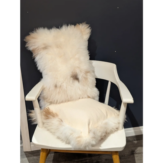 Fluffy off-white sheepskin throw pillow with soft natural fur resting on a white wooden chair by angus oliver canada