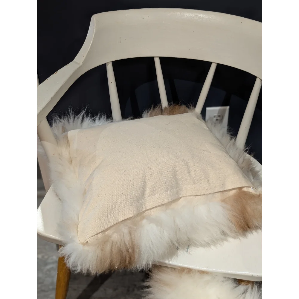 Cream-colored linen pillow resting on white chair with fluffy off-white sheepskin in adorable angus oliver canada set