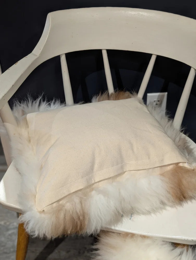 Cream-colored linen pillow resting on white chair with fluffy off-white sheepskin in adorable angus oliver canada set