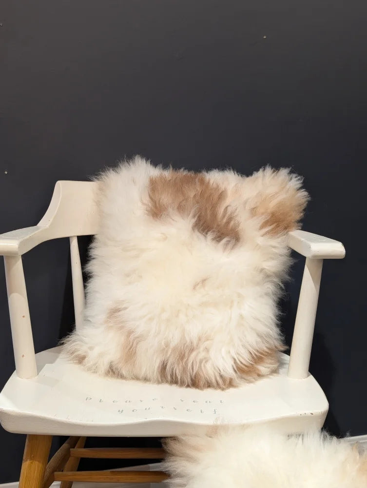 A fluffy cream and tan sheepskin throw pillow from angus oliver resting on a white chair perfect for canada homes