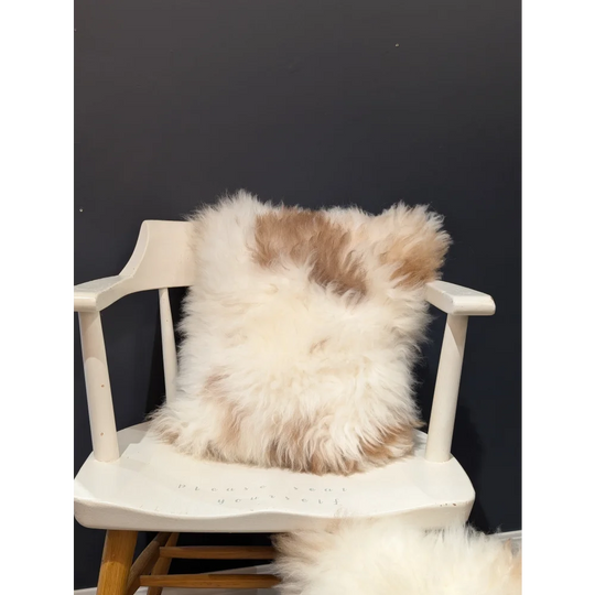 A fluffy cream and tan sheepskin throw pillow from angus oliver resting on a white chair perfect for canada homes