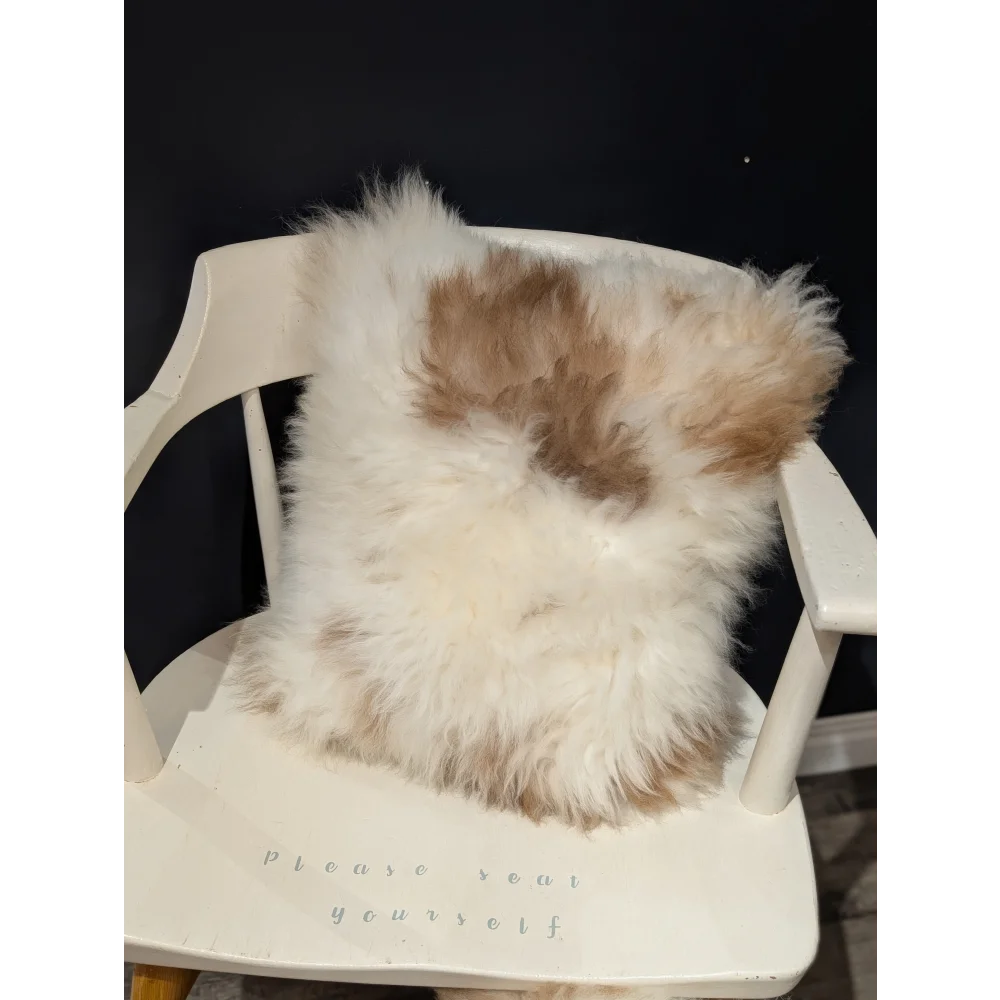 A fluffy cream and tan sheepskin pillow with soft natural texture on a white chair by angus oliver canada
