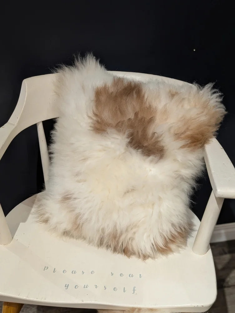 A fluffy cream and tan sheepskin pillow with soft natural texture on a white chair by angus oliver canada