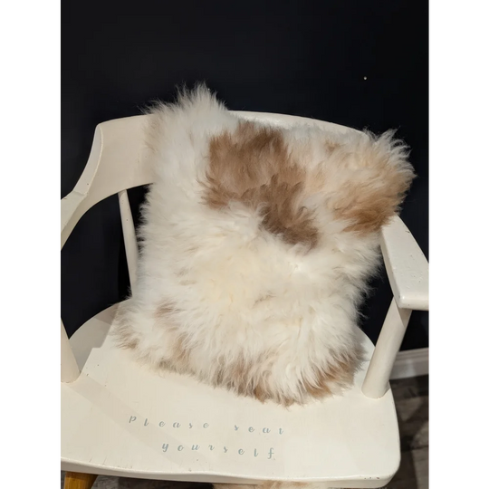 A fluffy cream and tan sheepskin pillow with soft natural texture on a white chair by angus oliver canada
