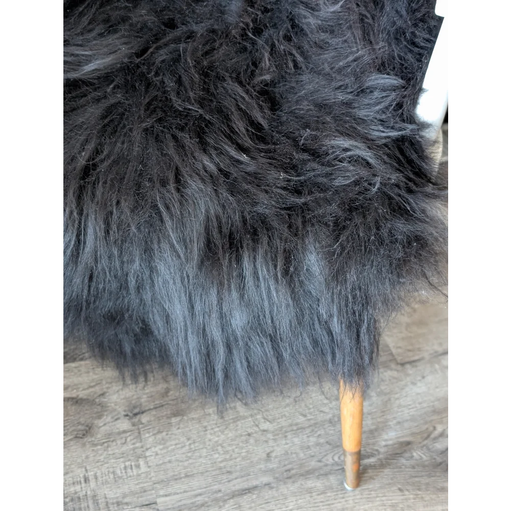 Black faux fur chair with wooden legs on soft Icelandic sheepskin rug
