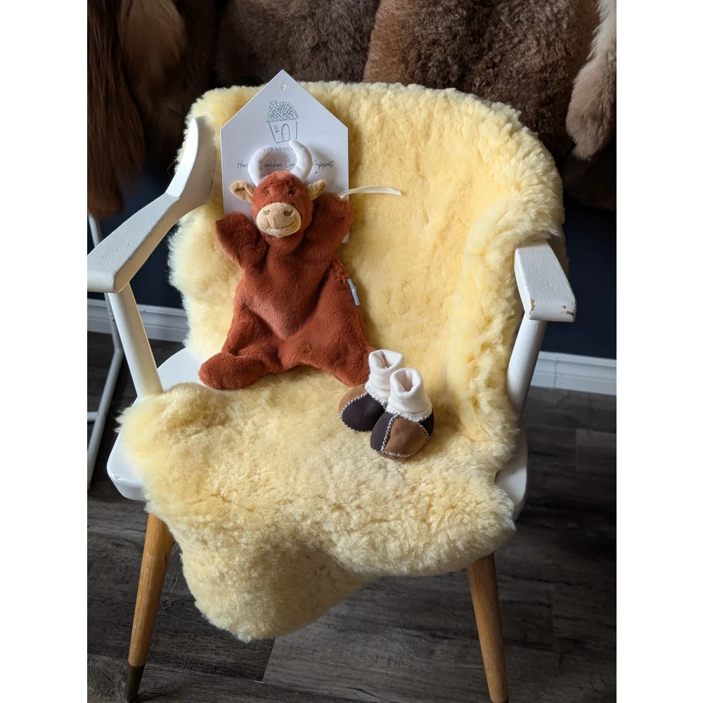 Brown plush Highland cow toy with white baby rattle and baby booties on medical sheepskin rug