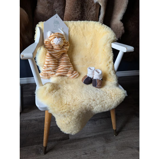White wooden chair with cream-colored medical sheepskin rug, plush toy, and baby booties