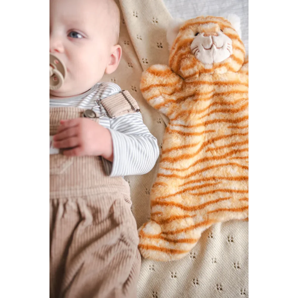 Cute baby with pacifier in striped jumpsuit lying next to tiger plush toy, soft medical sheepskin vibes