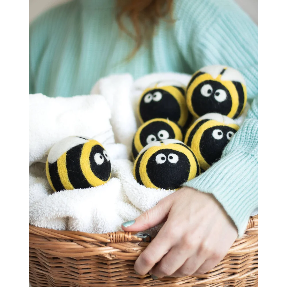 Bee trio eco wool dryer balls shaped like yellow and black bees with embroidered eyes in a white towel basket
