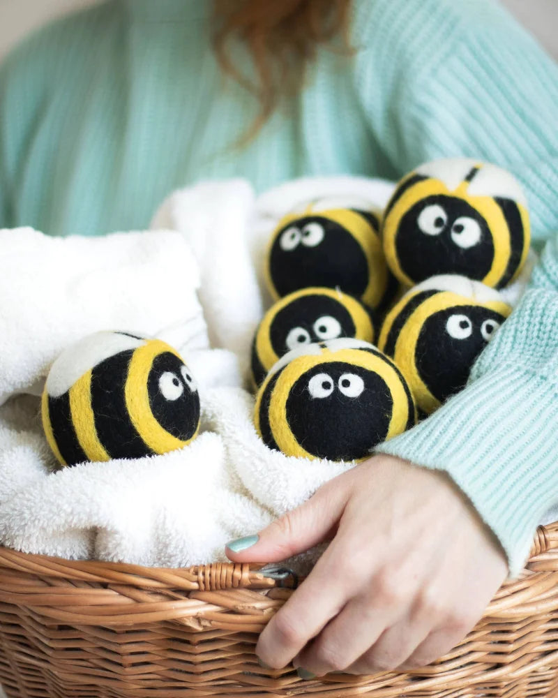 Bee trio eco wool dryer balls shaped like yellow and black bees with embroidered eyes in a white towel basket