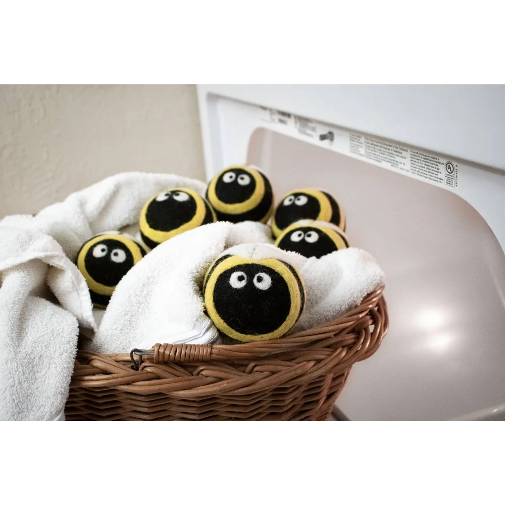 Yellow and black fuzzy bee trio eco wool dryer balls nestled in a wicker basket with white towels