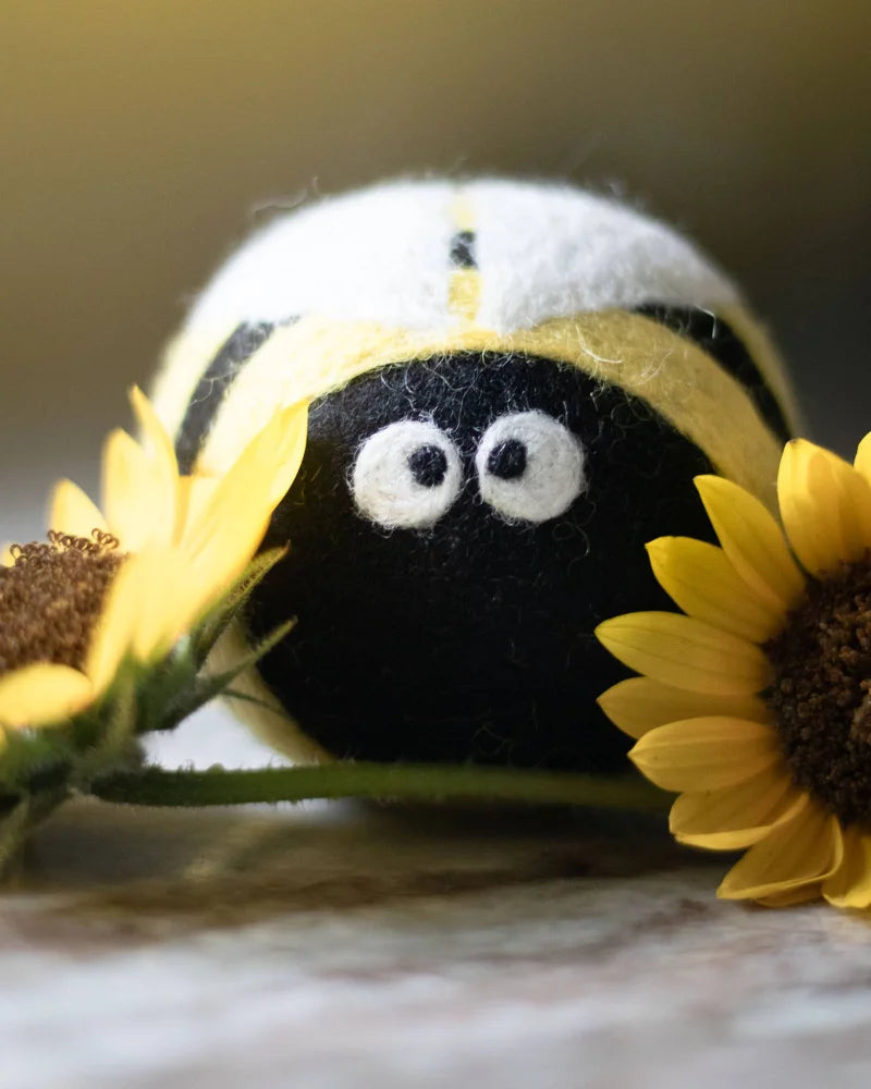A charming black and yellow eco dryer ball with embroidered white eyes from the bee trio set peeking out from sunflowers
