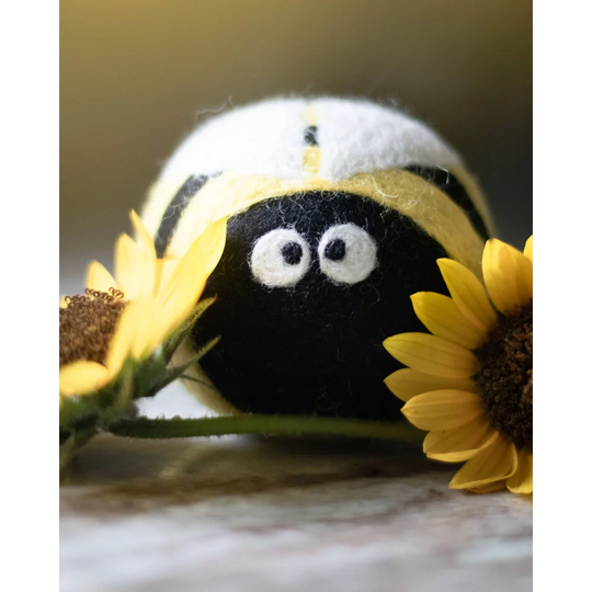 A charming black and yellow eco dryer ball with embroidered white eyes from the bee trio set peeking out from sunflowers