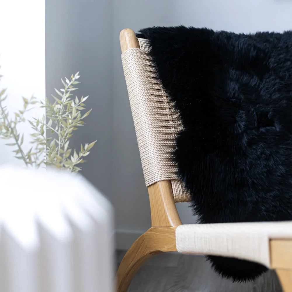 Black dyed merino sheepskins faux fur throw draped over wooden chair with woven rope backrest meeting european standards