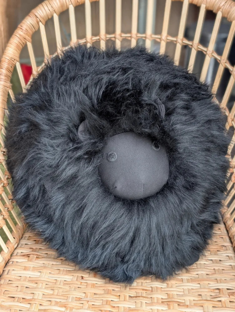 Black rotund sheepskin cushion with plush black fur and soft gray face made from merino sheepskin for cozy seating