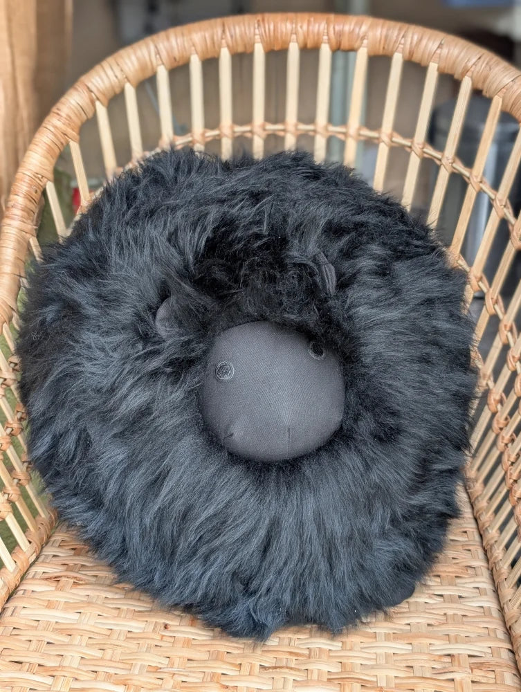 Black rotund sheep cushion made of soft merino sheepskin with fluffy texture and embroidered facial features