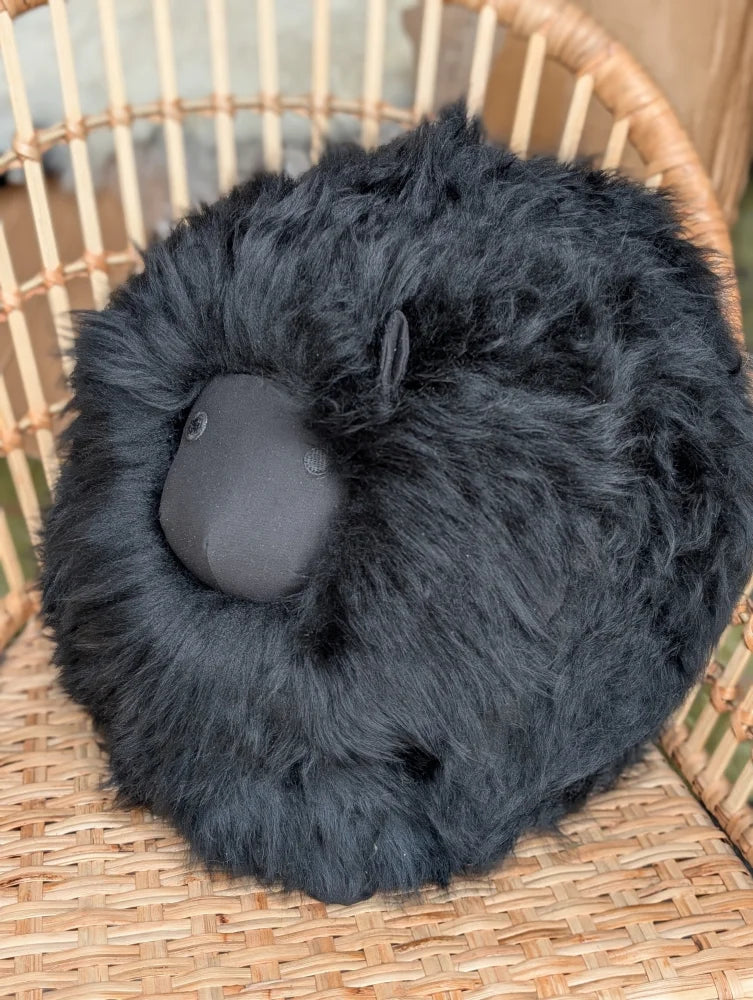 Black rotund sheep cushion with fluffy merino sheepskin fur and smooth matte face for cozy home decor