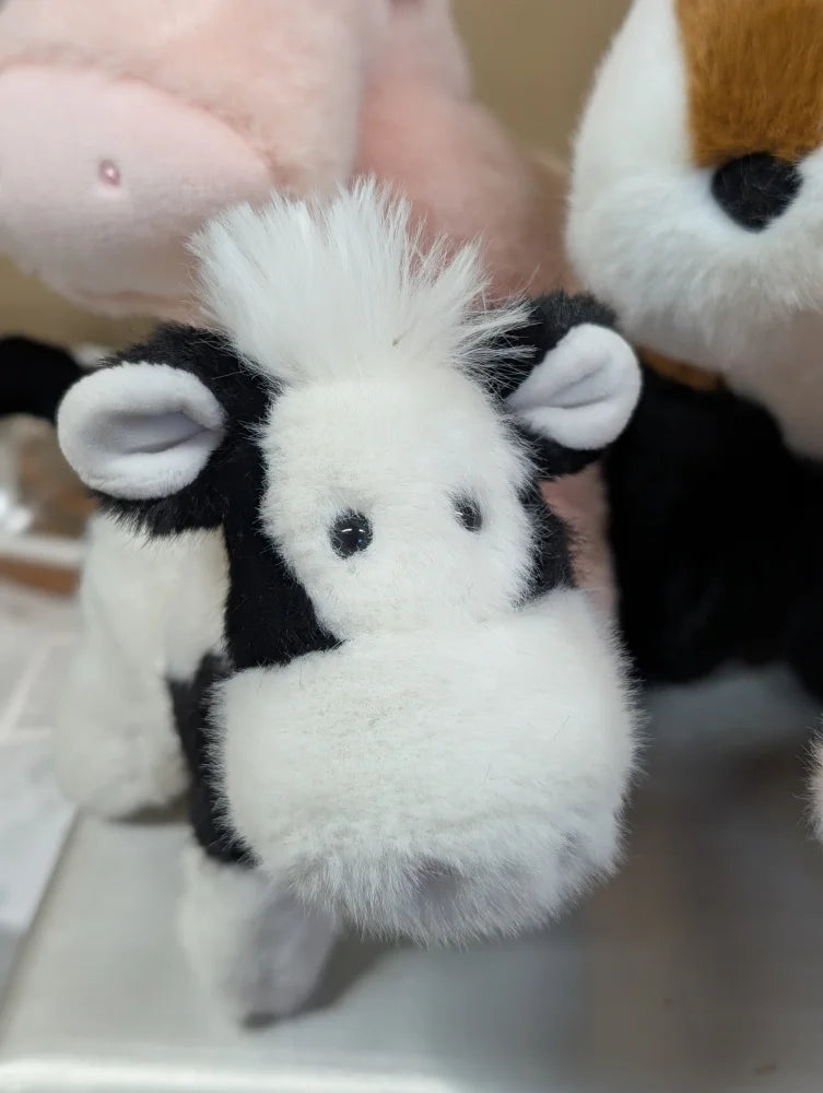 A plush black and white cow toy with fluffy fur soft ears and a rounded snout perfect for kids and decor