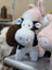 A plush black and white cow toy with soft fur pink nose details and stitched eyes perfect for cuddling