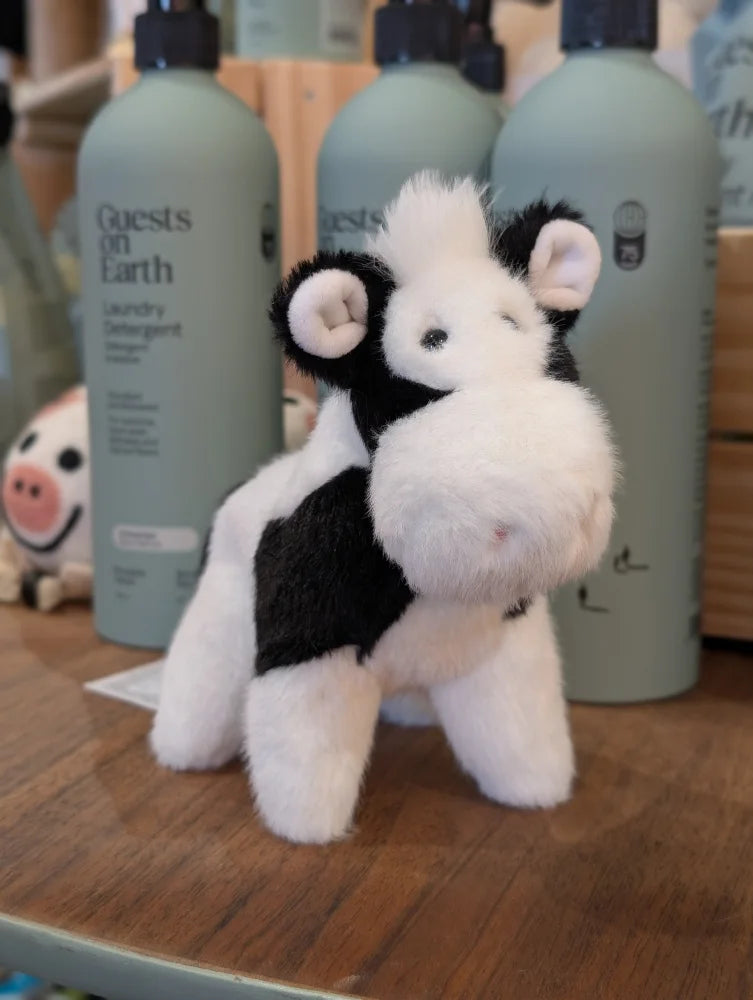 Black and white cow plush toy with soft fur and giant snuggly muzzle standing on wooden surface