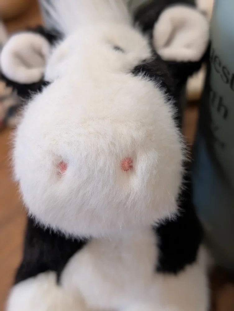 A plush black white cow toy with fluffy fur and a giant snuggly muzzle featuring soft pink nose details