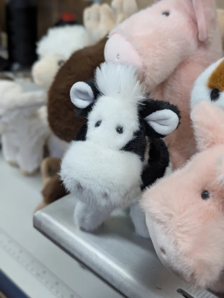 A plush black and white cow toy with soft fluffy fur and embroidered eyes perfect for cuddling and play