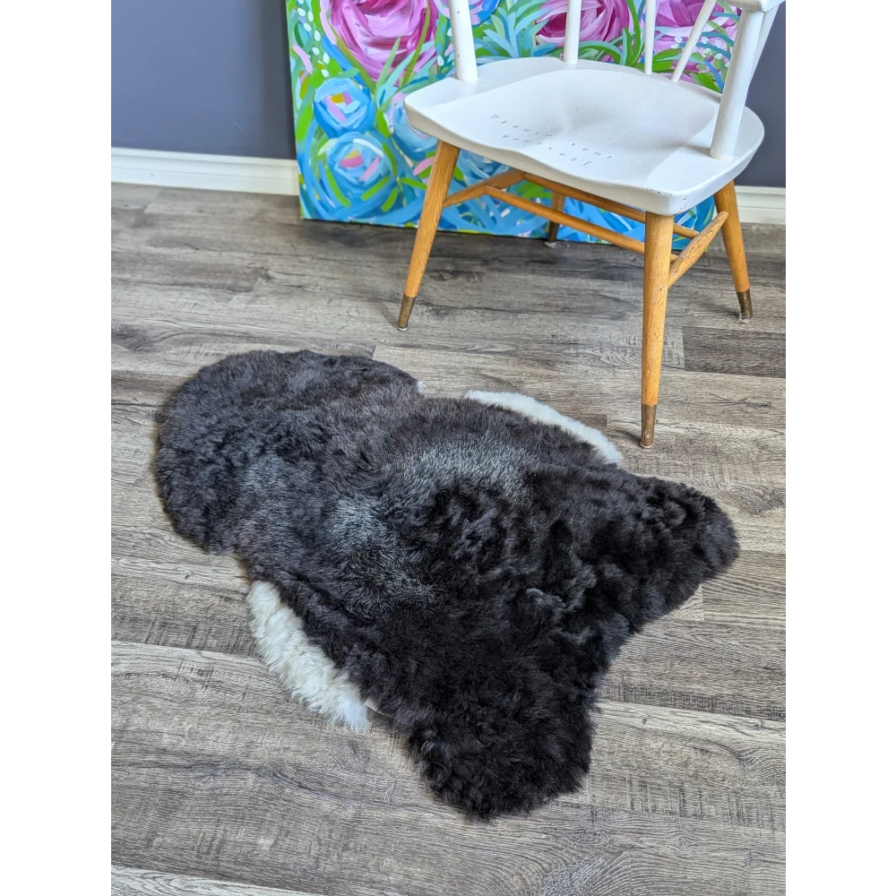 A plush irregular black with white sides icelandic sheepskin rug with soft medium spotted icelandic short wool texture on wood floor