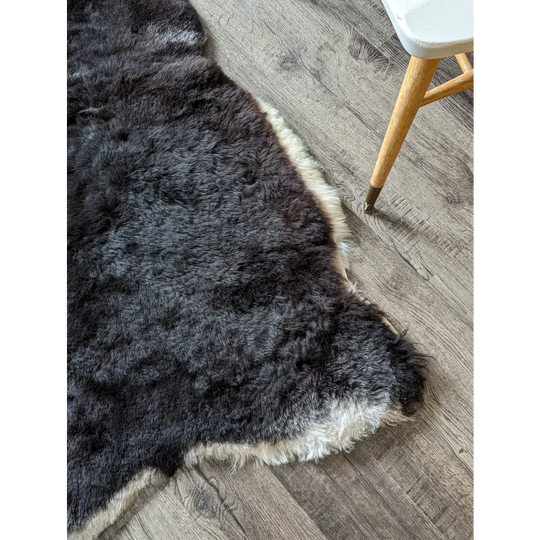 A black with white sides icelandic sheepskin rug featuring soft dark gray short wool and a plush white fur edge on wood floor