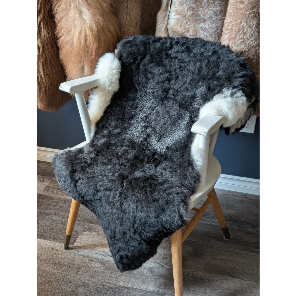 A plush dark gray icelandic sheepskin rug with white fur trim draped over the back of a wooden chair showing the back side