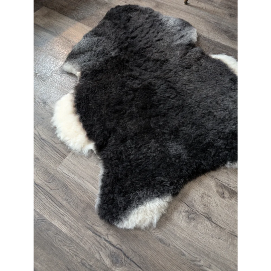 A plush black with white sides icelandic sheepskin rug with a soft medium spotted natural wool pattern